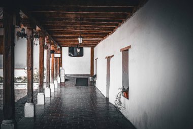 Bir tarafında duvar, diğer tarafında tahta sütunlar olan bir bina. Tavandaki kirişler