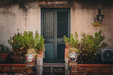 Kapısı ve ahşap yeşil gölgesi olan dış duvarlar inşa ediyor. Tuğla duvarlı veranda ve bitkilerle süslü Taormina kafaları.