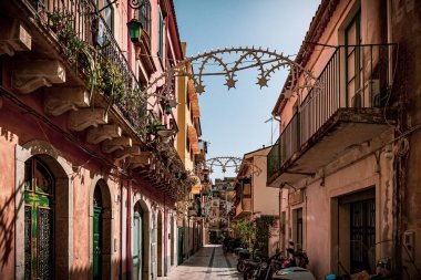 Balkonlu kırmızı duvar binaları ile Sicilya, Taormina 'daki saksı bitkileri arasındaki dar patika.