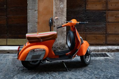 Portakallı scooter, duvarın yanına park etmiş Vespa boş asfalt sokakta ahşap kapılar.
