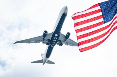 Delta Havayollarından gelen uçak arka planda Amerikan bayrağına karşı gökyüzünde uçuyor.