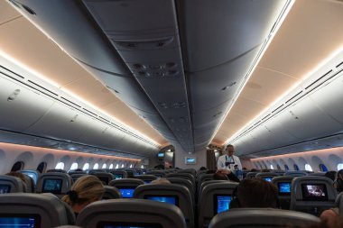 Roma, İtalya - 18 Ağustos 2023: Koltuklarda insanlar ve koridorda yürüyen üniformalı hosteslerin bulunduğu büyük yolcu uçaklarının içi