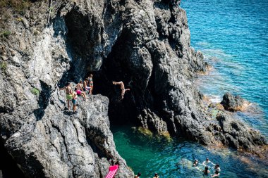 Monterosso, İtalya - 10 Temmuz 2023: Yüzme ve denize atlama zamanlarının tadını çıkaran bir grup insan
