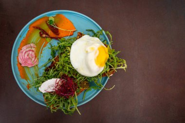 Haşlanmış yumurtalı tabak, yanında sosla birlikte yeşillerde servis edilir.