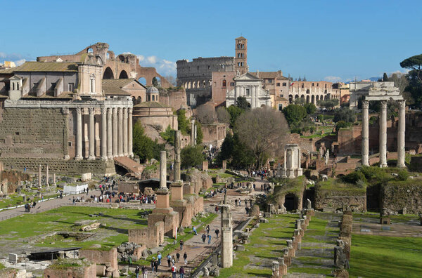 Majestic architecture fills the landscape of Rome, featuring the famous Colosseum and historical structures. Visitors admire these ancient sites on a sunny day.