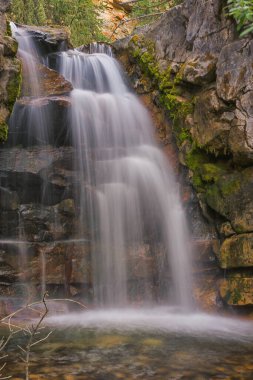 Kayalar ve yapraklarla çerçevelenmiş bir şelalenin portre manzarası sinekkuşu tüyü gözcü yürüyüşü, Kananaskis, Alberta