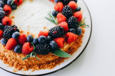 Homemade honey cake with fresh berries on top on a white wall background