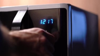 Mans hand twists microwave timer button, counts back. 