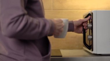 Man puts cup in microwave standing on table in home kitchen. 