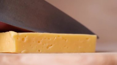 Knife in mans hand cuts yellow cheese with holes in cubes and slices. 