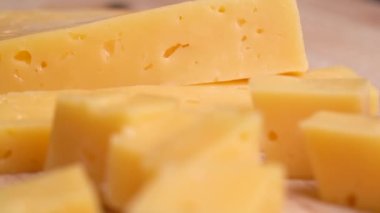 Camera moves along slice of yellow cheese with holes on cutting board. 