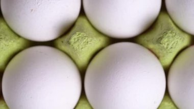 White chicken eggs rotate in green cardboard container, top view. 