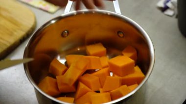 Mans hand throws cut pumpkin cubes into cooking pot. 