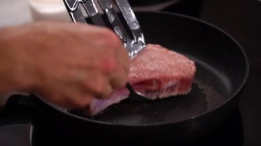 Hands turn over meat steak, meat on bone in a frying pan, frying. 