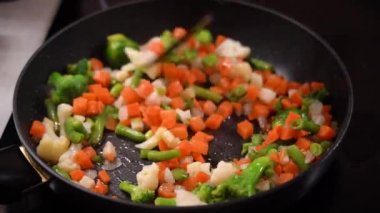 Frozen chopped vegetables are cooked in frying pan and stirred with spatula. 