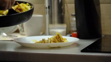 Apply fried potatoes from the pan to the plate, in the kitchen. 