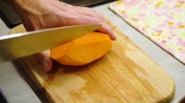 Mans hand cuts an orange pumpkin on cutting board into slices. 