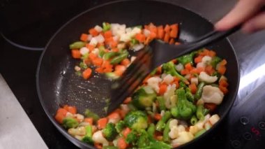 Frozen chopped vegetables are cooked in frying pan and stirred with spatula. 