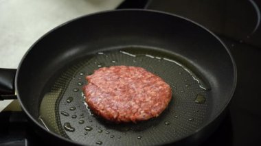 Burger cutlet is turned over with spatula and fried in frying pan. 