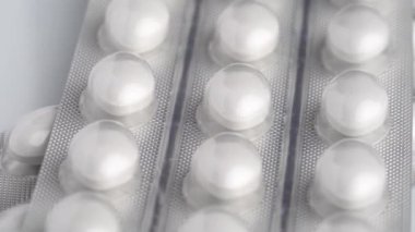 White tablets in blister rotate on white background, macro close-up. 