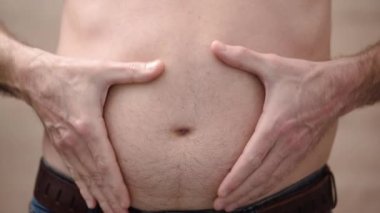 Man collects folds of fat on his stomach with his hands standing directly to camera. 