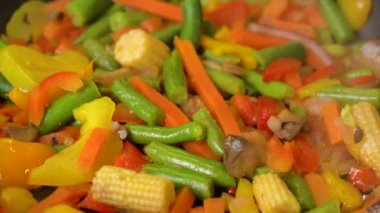 Frozen vegetables cooked in frying pan, steam rises, close-up. 