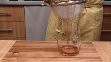 Bir adam, bir elek içinden cam sürahiye hamurla içki döker.. 