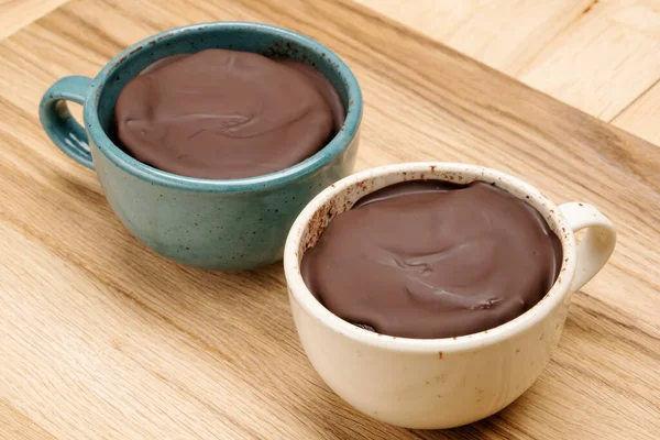 Chocolate dessert in cups of different colors standing on a wooden table.