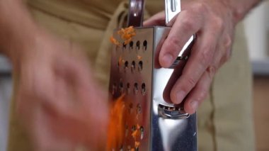 Erkek eli metal rendeleyiciye soyulmuş havuç sürer.. 