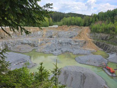 Yazın madencilik yapan bir taş ocağı. Dağlarda taş ocağı, orman, gökyüzü, bulutlar.