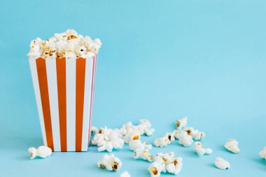 Kırmızı ve beyaz patlamış mısır kutusu ve mavi arka planda patlamış mısır. Kopya alanı ile TV izleme kavramı. Film gecesi. Eğlence konsepti.