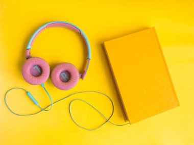 Sarı arka planda kitap ve kulaklık yığını. Audiobook konsepti. Dersleri dinle..