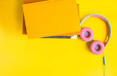Sarı arka planda kitap ve kulaklık yığını. Audiobook konsepti. Dersleri dinle..