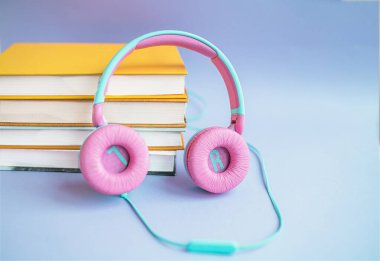 Mor bir arka planda kitap ve kulaklık yığını. Audiobook konsepti. Dersleri dinle..