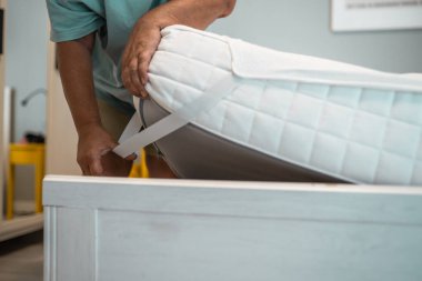 Mature woman changes a new clean mattress topper on a bed. Home duties concept.	