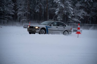 12-12-2022 Riga, Letonya. Önünde kırmızı ve beyaz bir trafik konisi olan karla kaplı bir orman bölgesinden geçen bir araba.. .