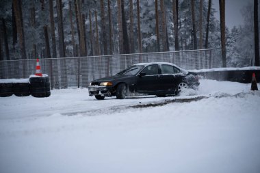 12-12-2022 Riga, Letonya Karlı bir yolda ilerleyen bir araba Ağaçlarla ve konilerle dolu bir ormanın yanında. .