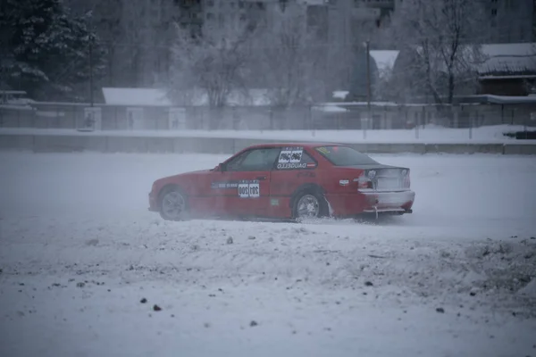 2012年12月12日から2022年までの間 ラトビアのリガは 冬に雪に覆われた駐車場を走る赤い車で 車の後ろに標識があります — ストック写真