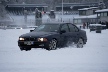 12-12-2022 Riga, Letonya. Karla kaplı bir otoparkta giden bir araba. Arka planda yürüyen insanlar ve arka planda bir bina var.. .