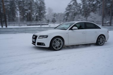 12-12-2022 Riga, Letonya. Karla kaplı yolda ilerleyen beyaz bir araba. Ağaçlardan oluşan bir ormanın yanında.. .