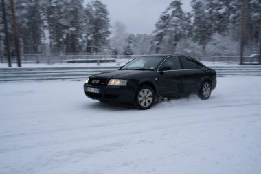 12-12-2022 Riga, Letonya. Bulutlu bir günde karlı bir yolda ilerleyen bir araba. Arka planda ağaçlar ve ön planda bir çit var.. .