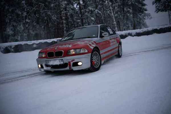 2012年12月12日 2022年リガ ラトビア雪に覆われた道路を運転する赤と白の車の背景に木といくつかの雪で覆われた地面 — ストック写真