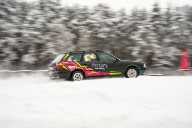 12-12-2022 Riga, Letonya. Arka planda ağaçlar ve ön planda kırmızı bir direk olan kar tarlasından geçen bir araba.. .