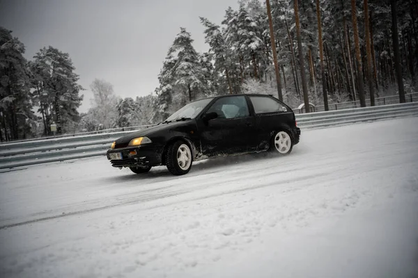 stock image 12-12-2022 Riga, Latvia a small car driving down a snowy road in the snow with trees in the background and a fence in the foreground. .