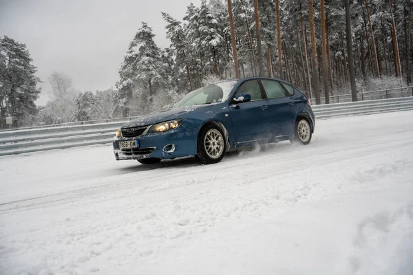 stock image 12-12-2022 Riga, Latvia a blue car driving down a snow covered road next to a forest of trees and a fence with snow on it. .