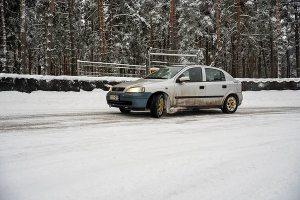 stock image 12-12-2022 Riga, Latvia a car driving down a snowy road in front of a forest of trees and a fence with snow on it. .