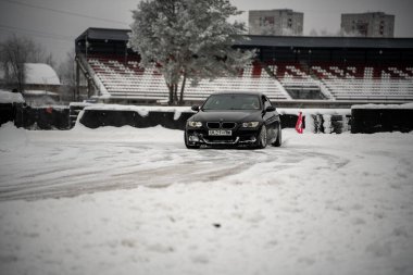 12-12-2022 Riga, Letonya. Arka planda bir kişi ve arka planda bir binanın bulunduğu bir stadyumun yakınındaki karlı bir yolda ilerleyen bir araba.. .