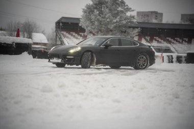 12-12-2022 Riga, Letonya. Kışın bir stadyumun yakınına park edilmiş bir araba. Yerde kar ve arka planda bir bina var.. .