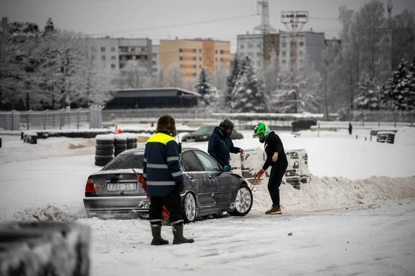 12-12-2022 Riga, Letonya. Kaputunda kar püskürtücüsü olan bir araba etrafında duran bir grup insan.. .