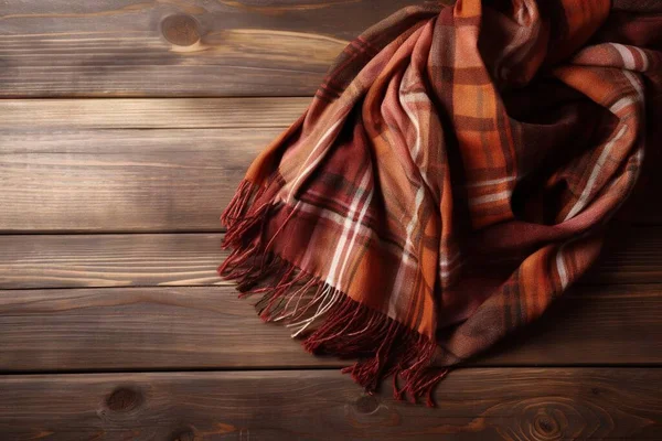 a plaid scarf is laying on a wooden surface with a wooden background and a wood grained wall in the backround of the photo.